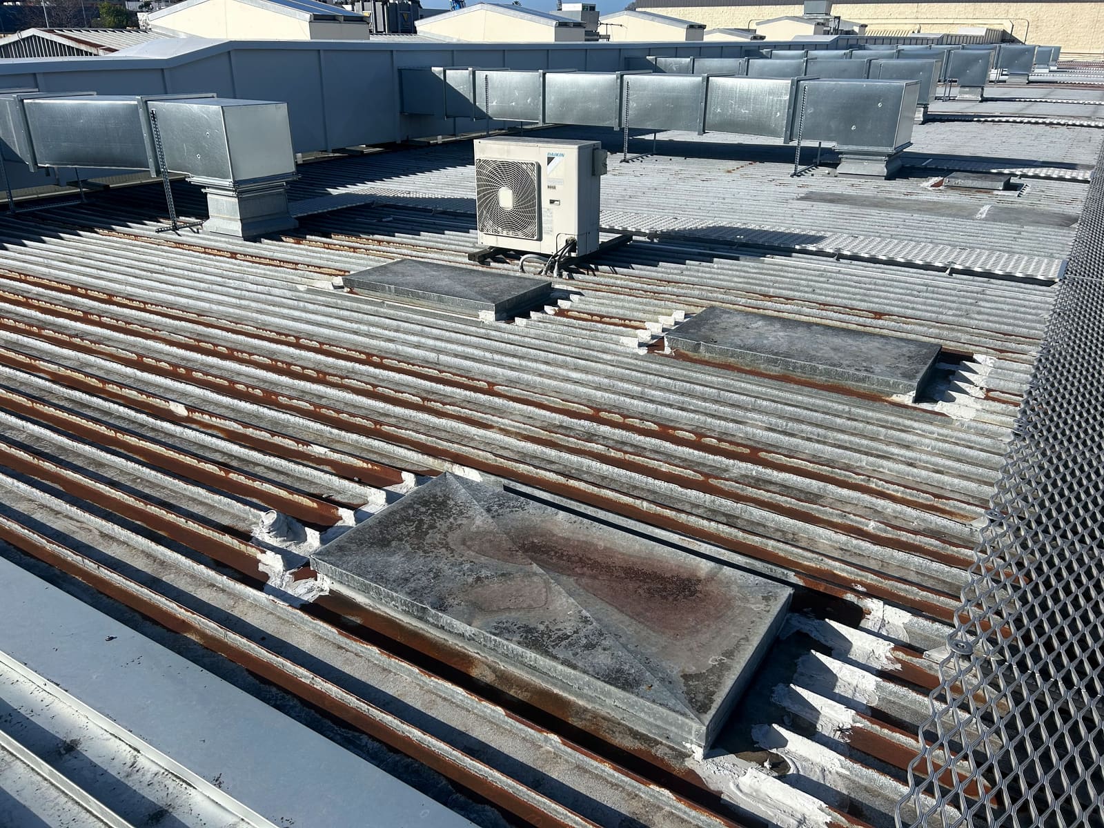 An existing commercial corrugated roof with heavy rust along the ribs and capped penetrations.