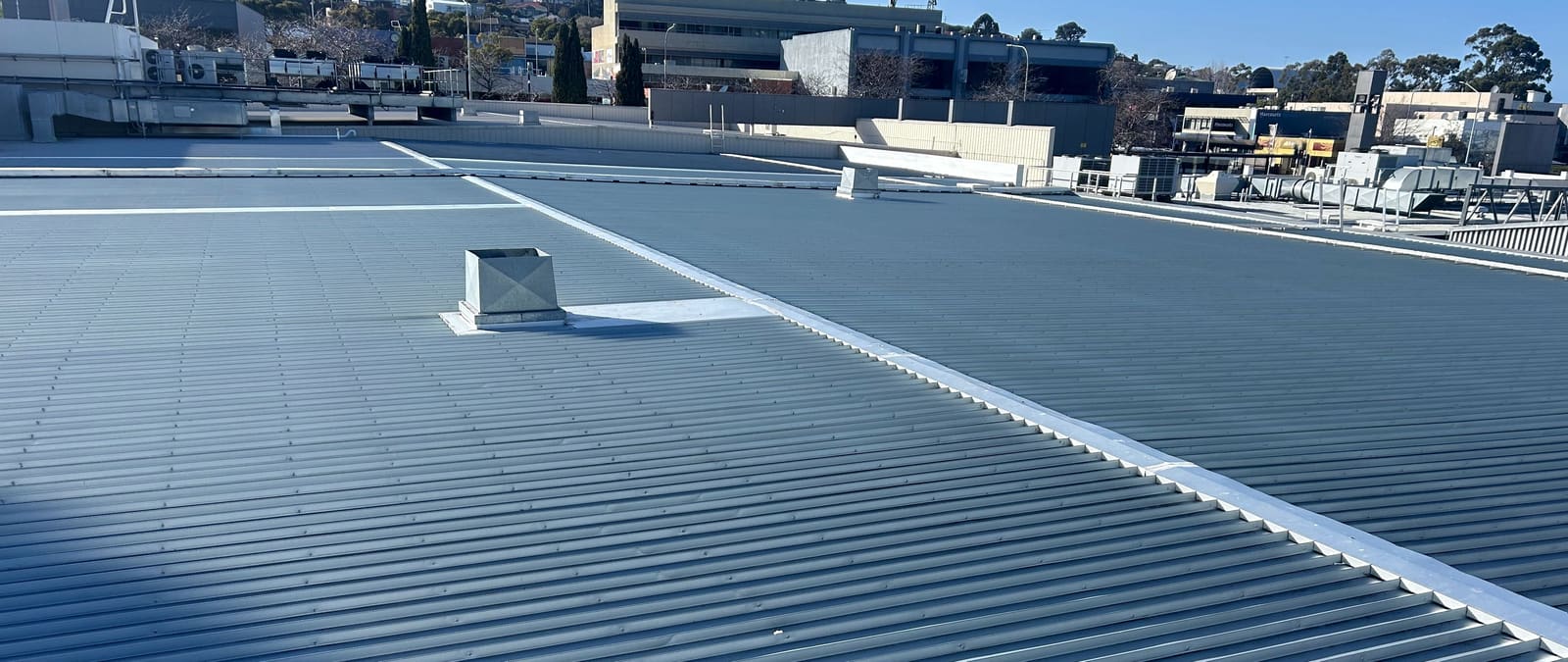 A large new corrugated metal roof running to the ridge on a commercial building, with the city and hills behind.
