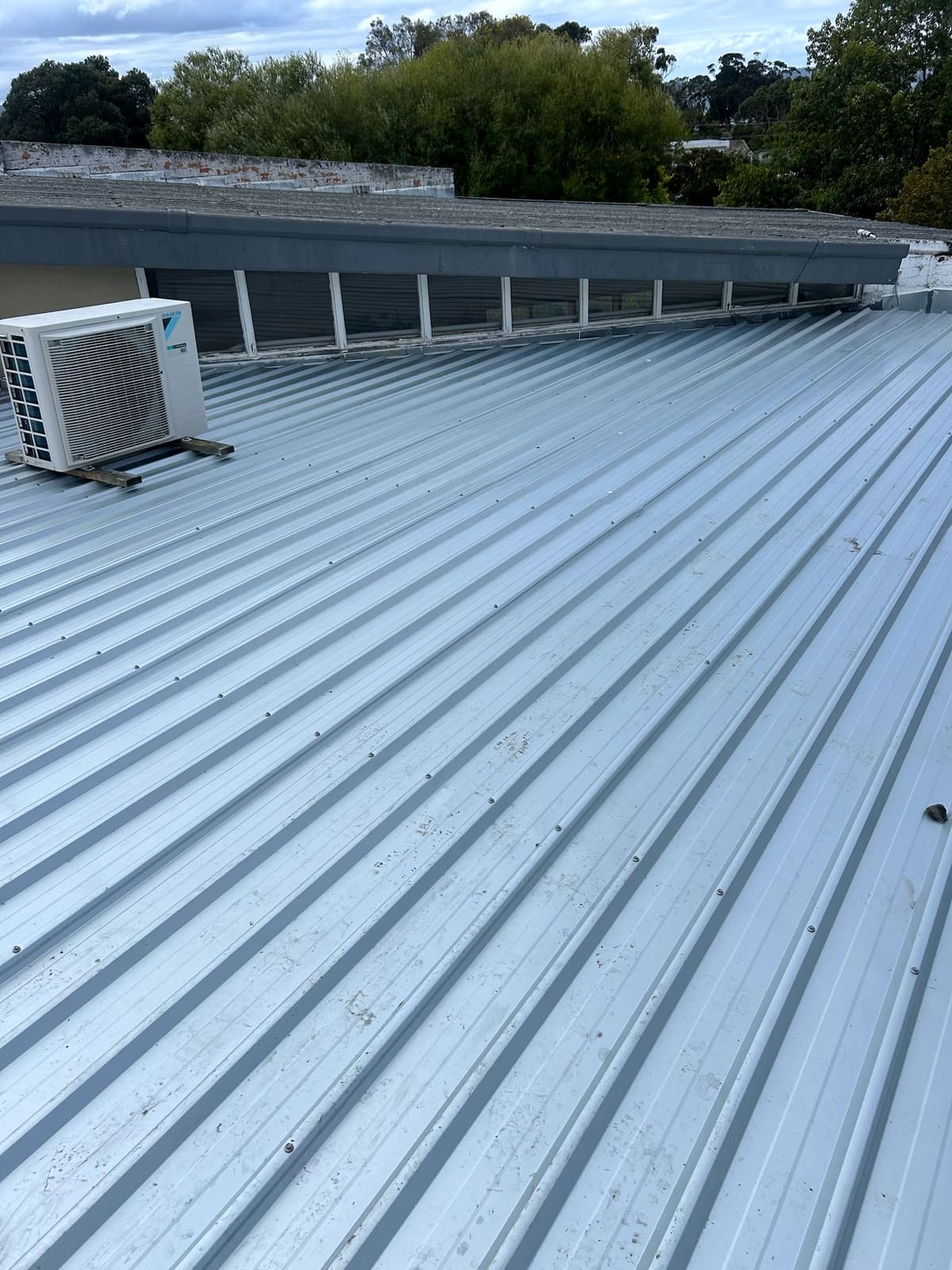 New pale square-rib metal roof behind a parapet, with clerestory windows and a plant unit.