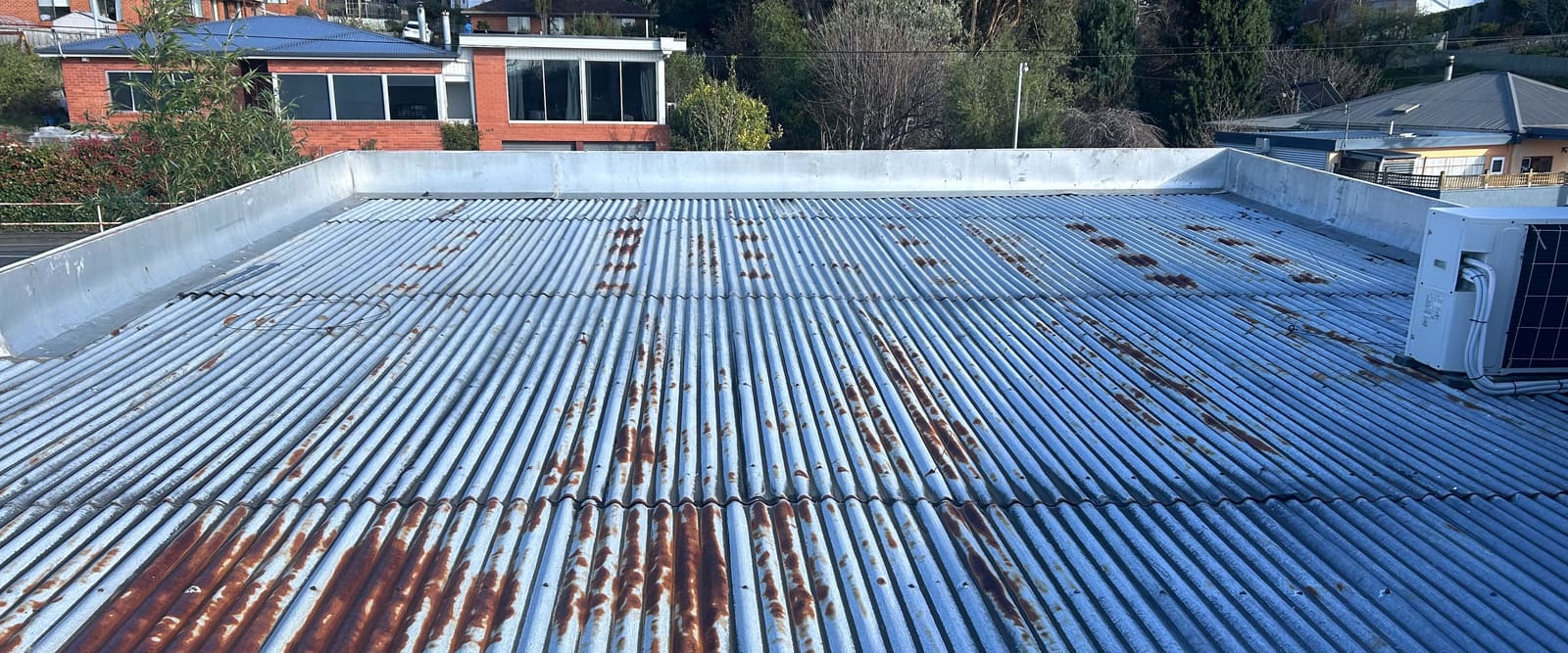 An existing corrugated metal roof with heavy rust staining, behind a parapet.