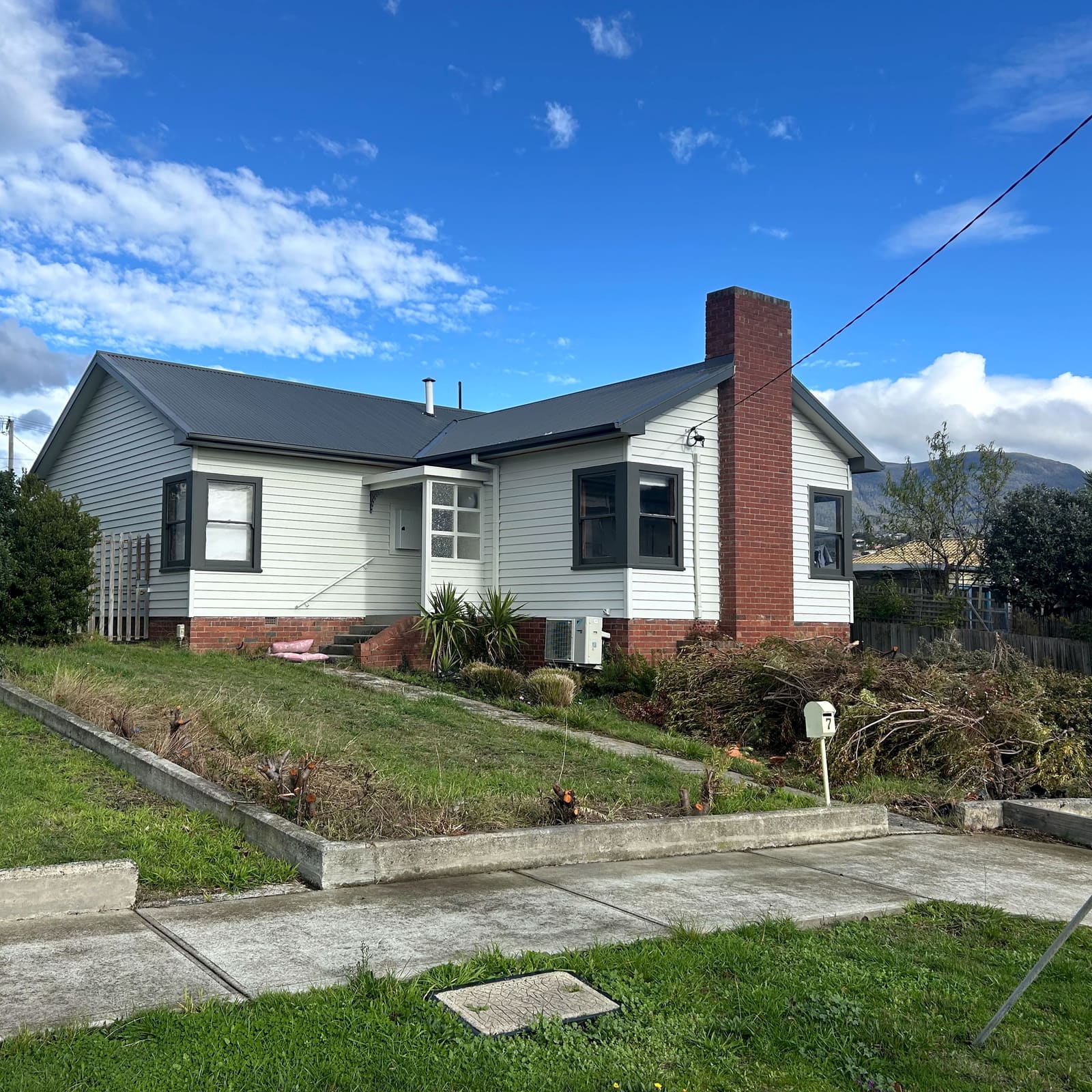 Weatherboard house with a newly installed dark corrugated metal roof and matching gutters, hills behind.